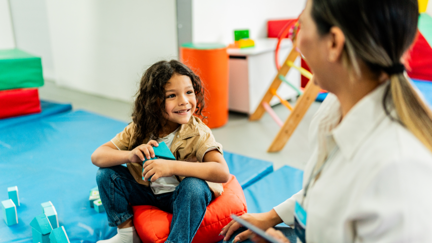 Child smiling and interacting with a clinician in a colorful therapy setting.