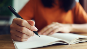 Person writing notes in an open notebook at a desk.
